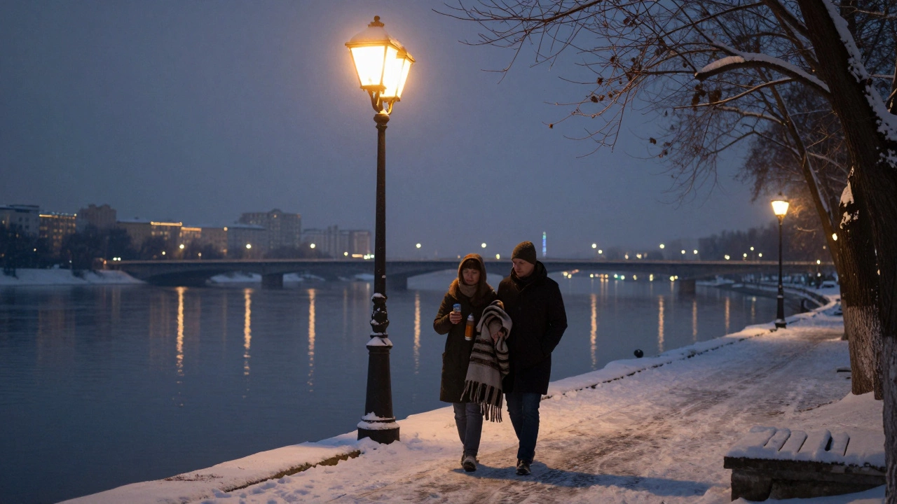 Пара гуляет по набережной в сумерках, держит термос чая и плед, городские огни позади.